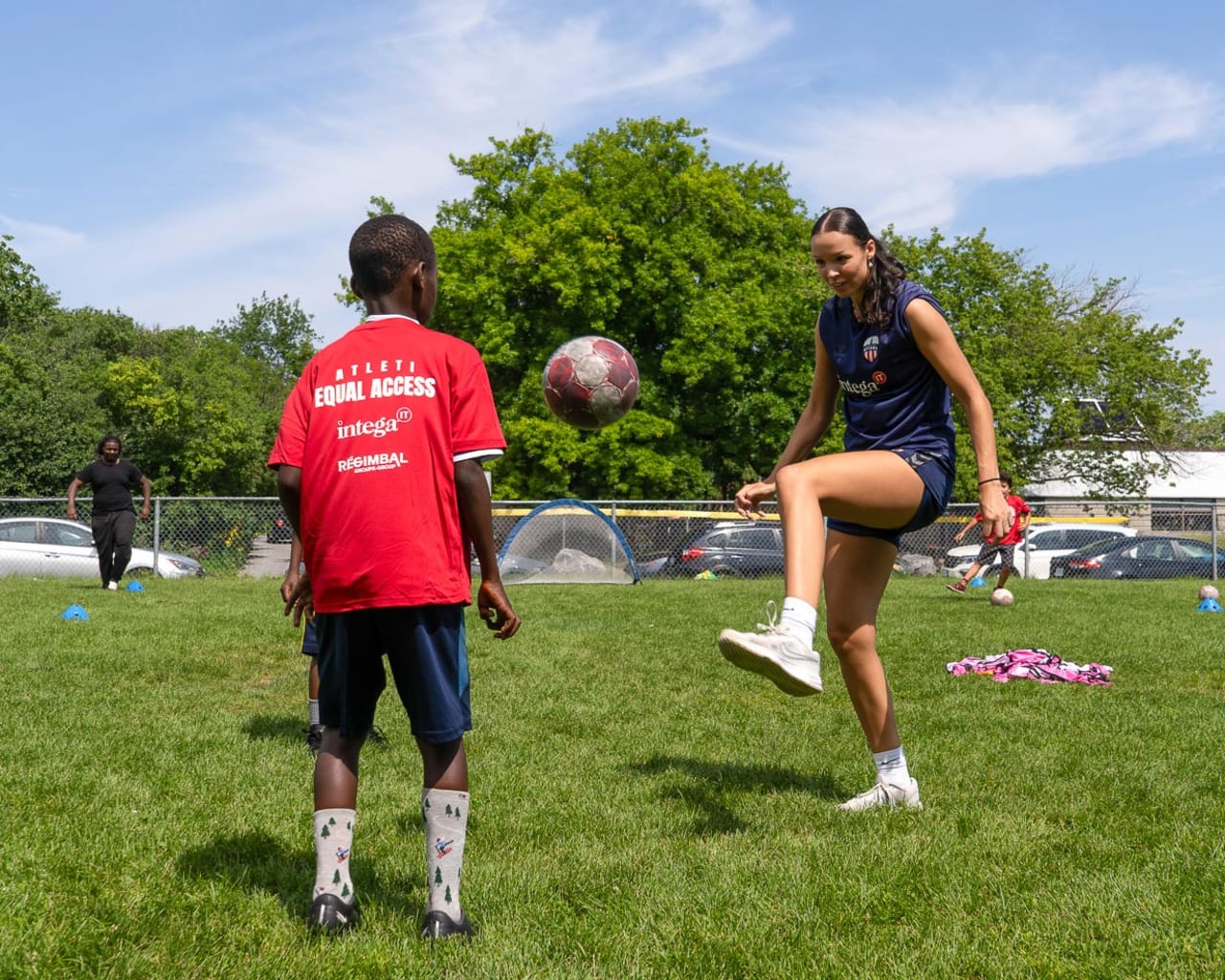 Female soccer coach playing soccer with young camper in a red t-shirt
