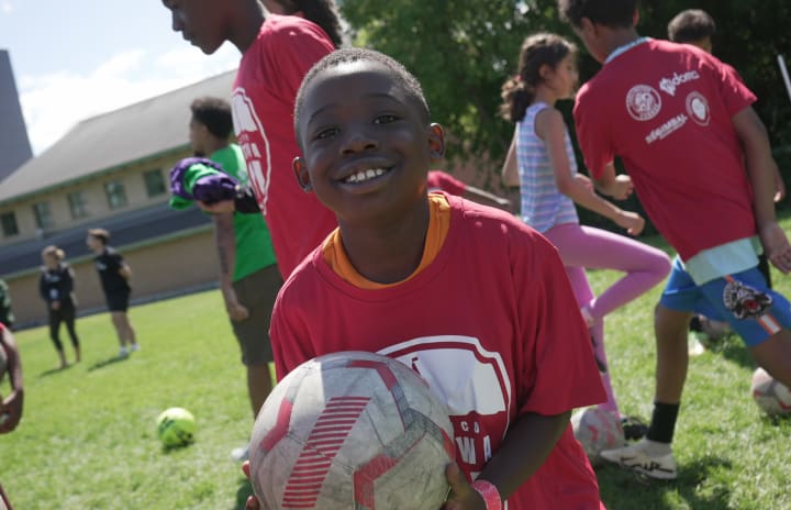 Young boy smiles at camera while holding a soccer ball
