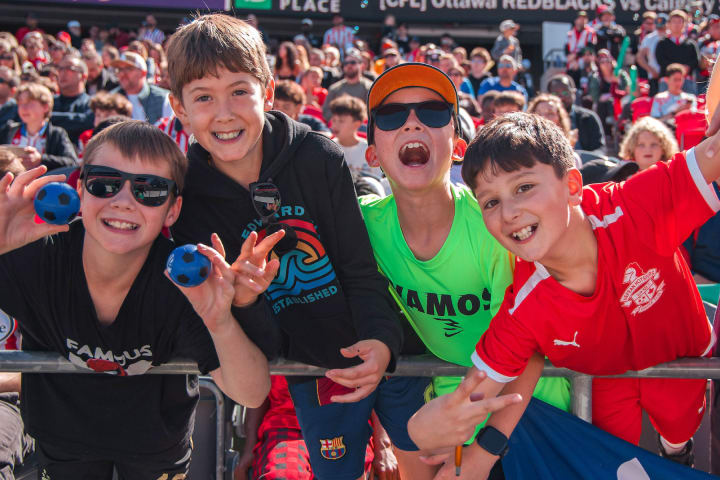 Four kids smiling at the camera in a stadium